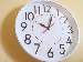 A wall clock with a white face and bold black numbers showing the time as just after 11 o'clock, mounted on a beige wall, symbolising time management or productivity.