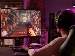 A teenager wearing headphones plays a first-person shooter video game on a computer monitor, representing xAI hiring human tutors to help train its AI, Grok, in game design.