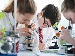 Secondary school students in uniform concentrating on a science experiment using microscopes in a classroom laboratory.